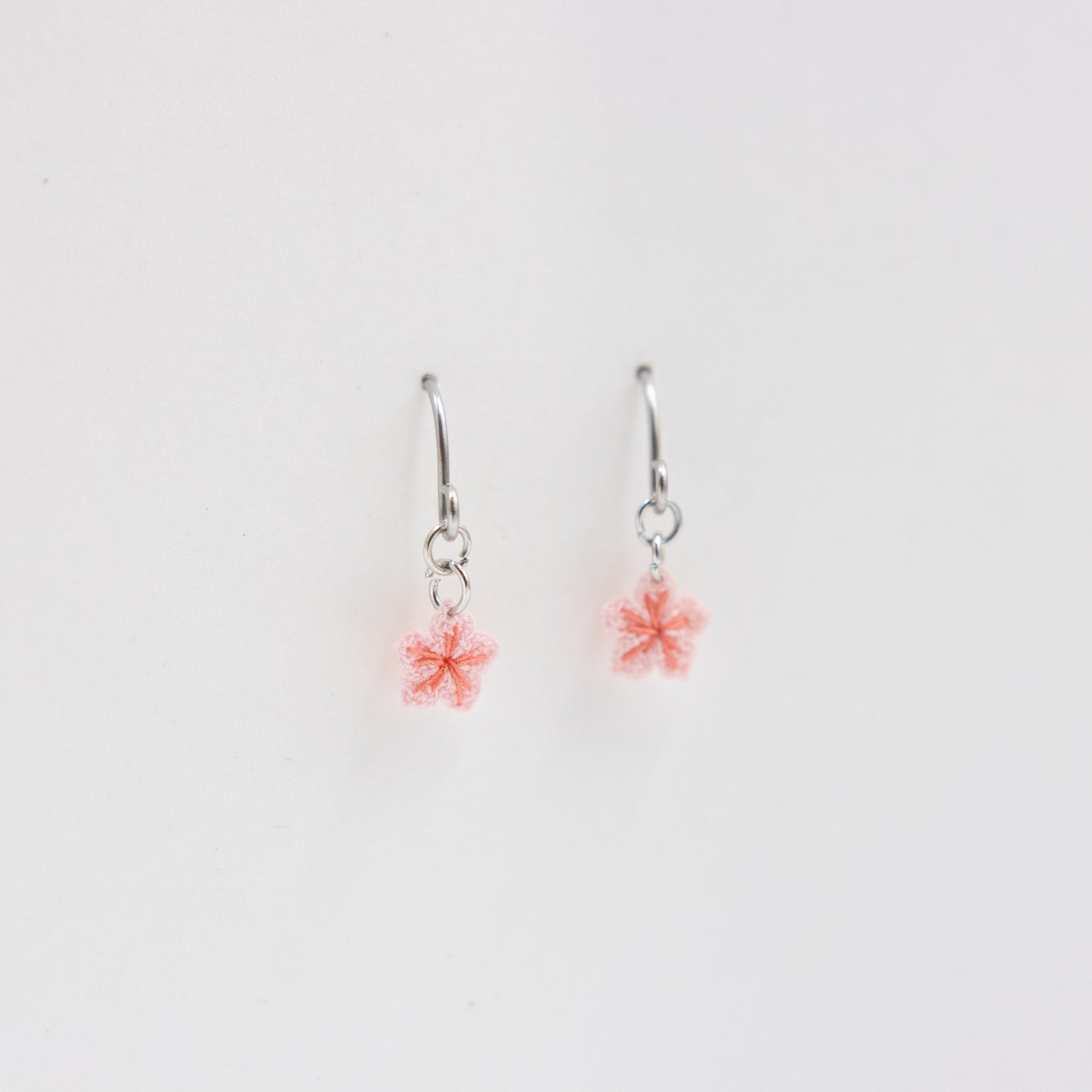 Pair of silver earrings with pink flower charms on a light gray background