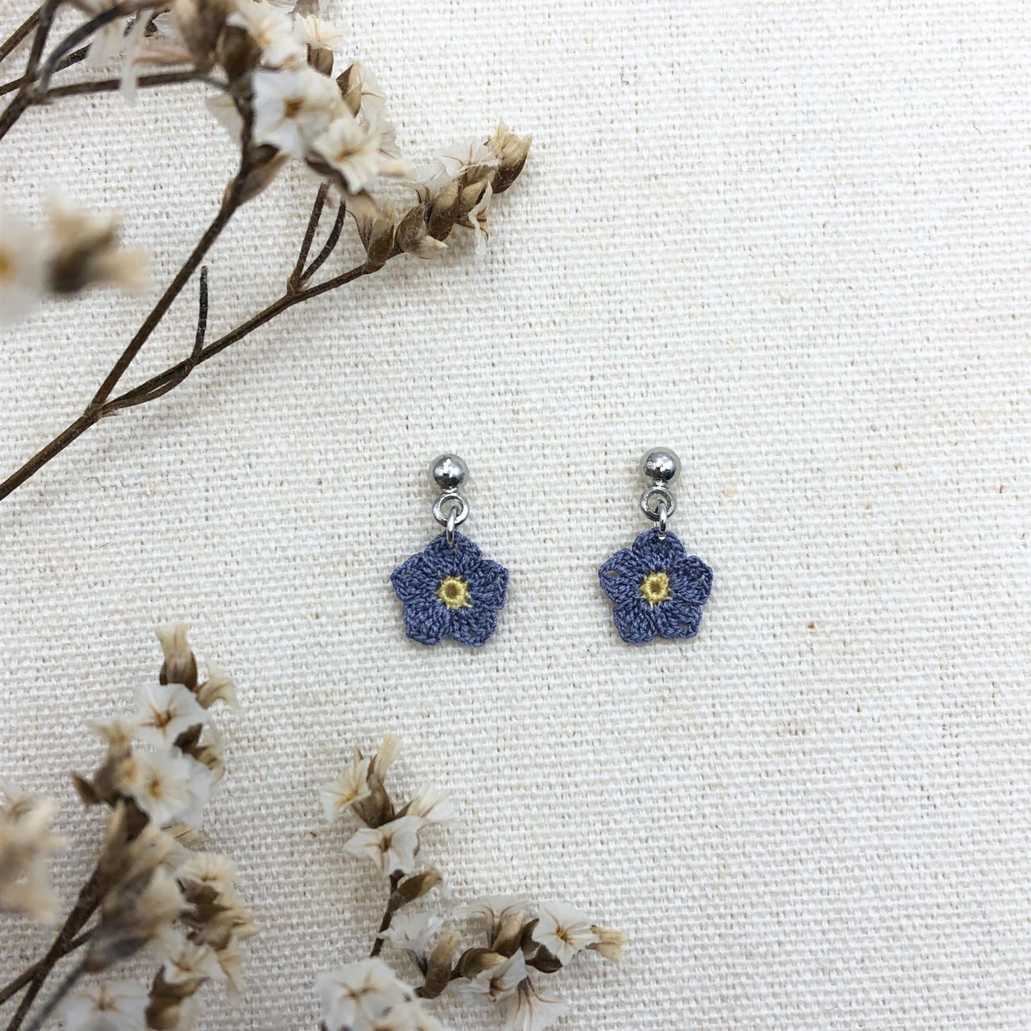 Blue flower-shaped earrings on a white background with dried flowers.