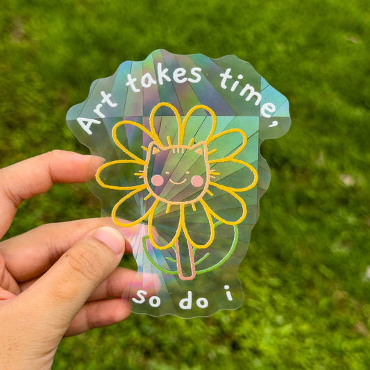 Holographic sticker with a sunflower design and text held against a grass background