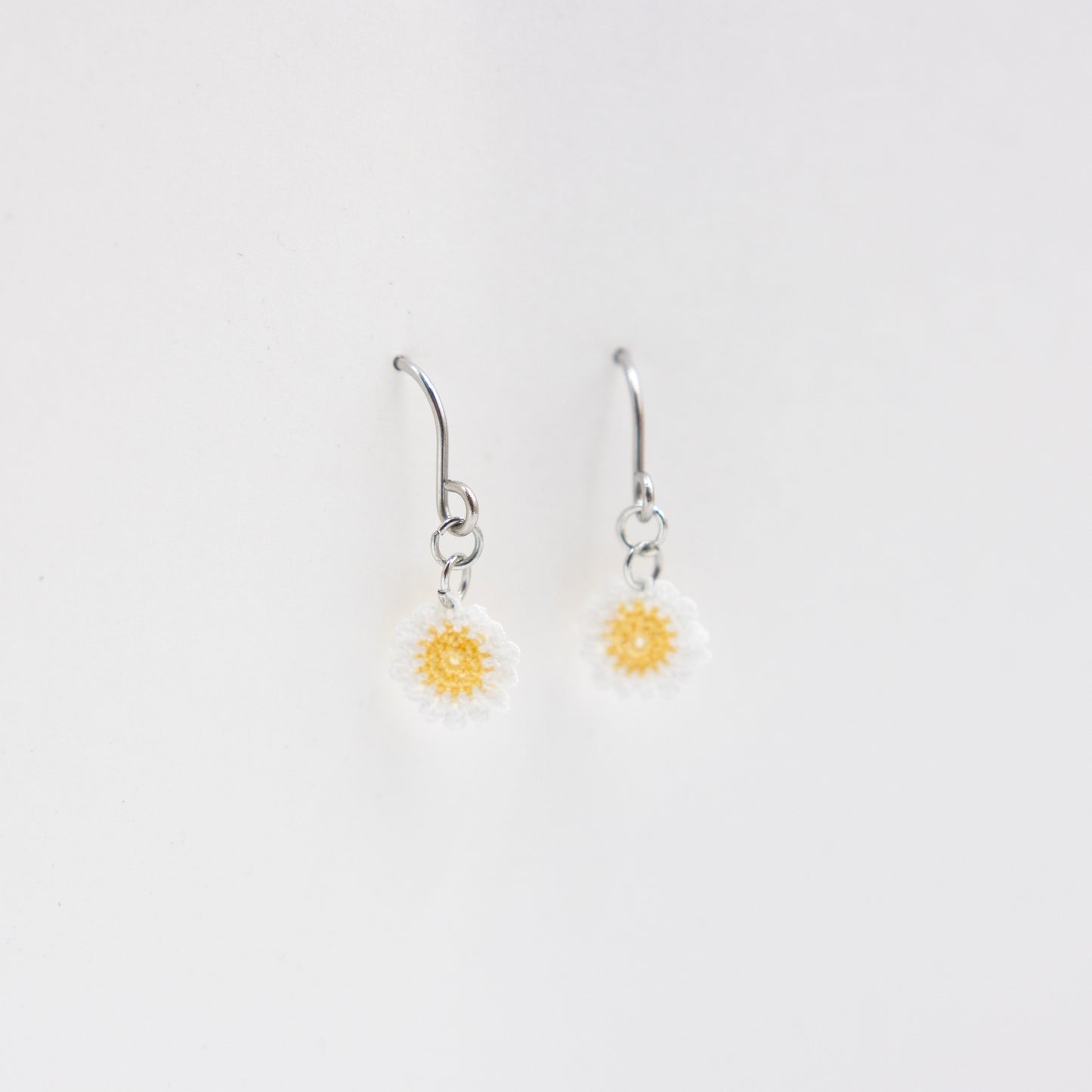 Pair of silver earrings with yellow flower charms on a light gray background