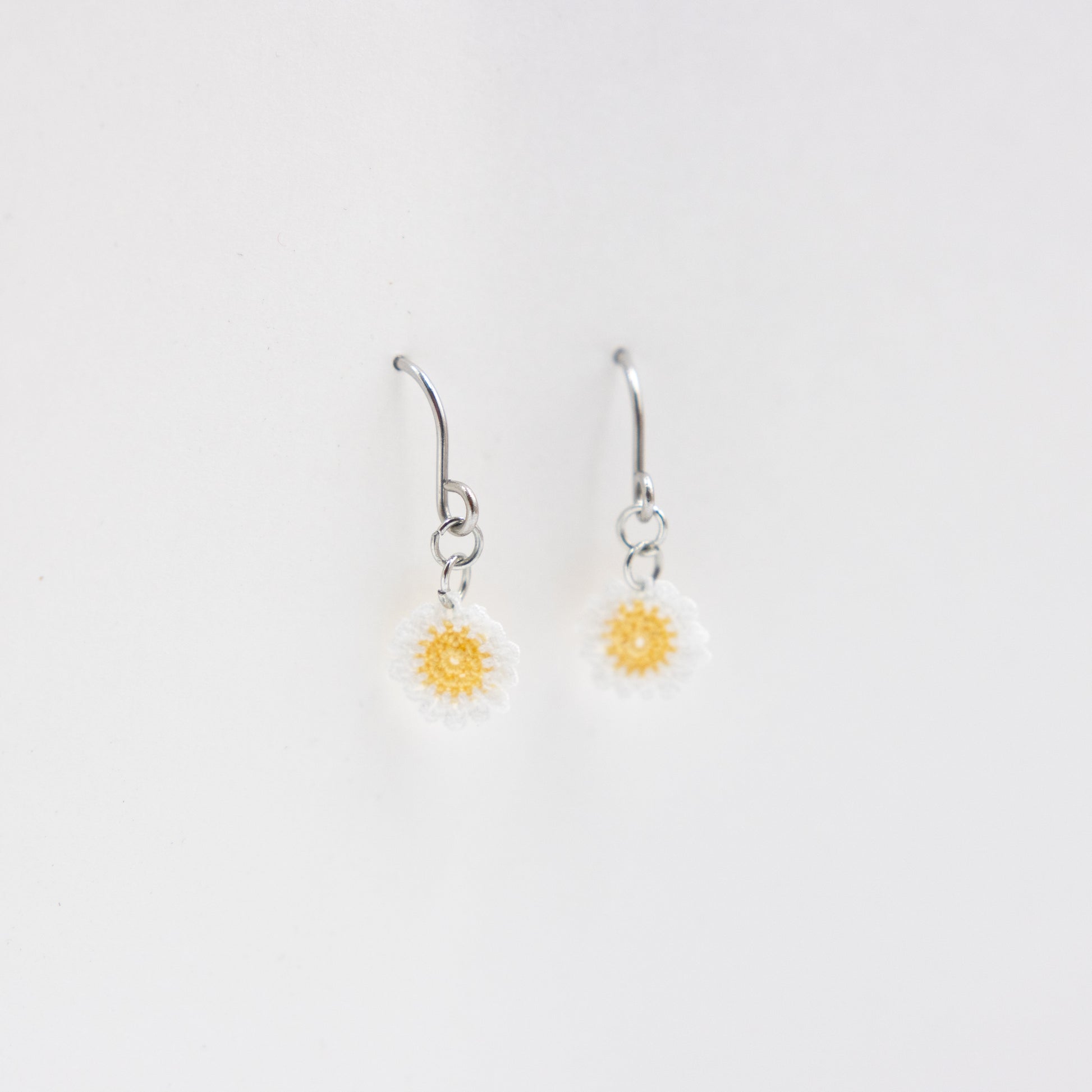 Pair of silver earrings with yellow flower charms on a light gray background