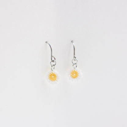Pair of silver earrings with yellow flower charms on a light gray background