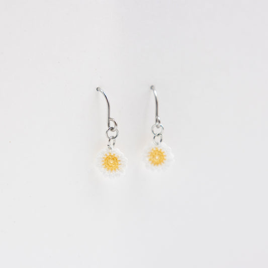 Pair of silver earrings with yellow flower charms on a light gray background