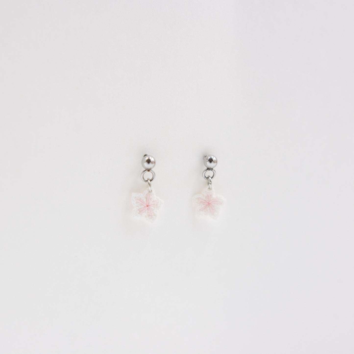 Pair of silver earrings with pink floral charms on a light gray background