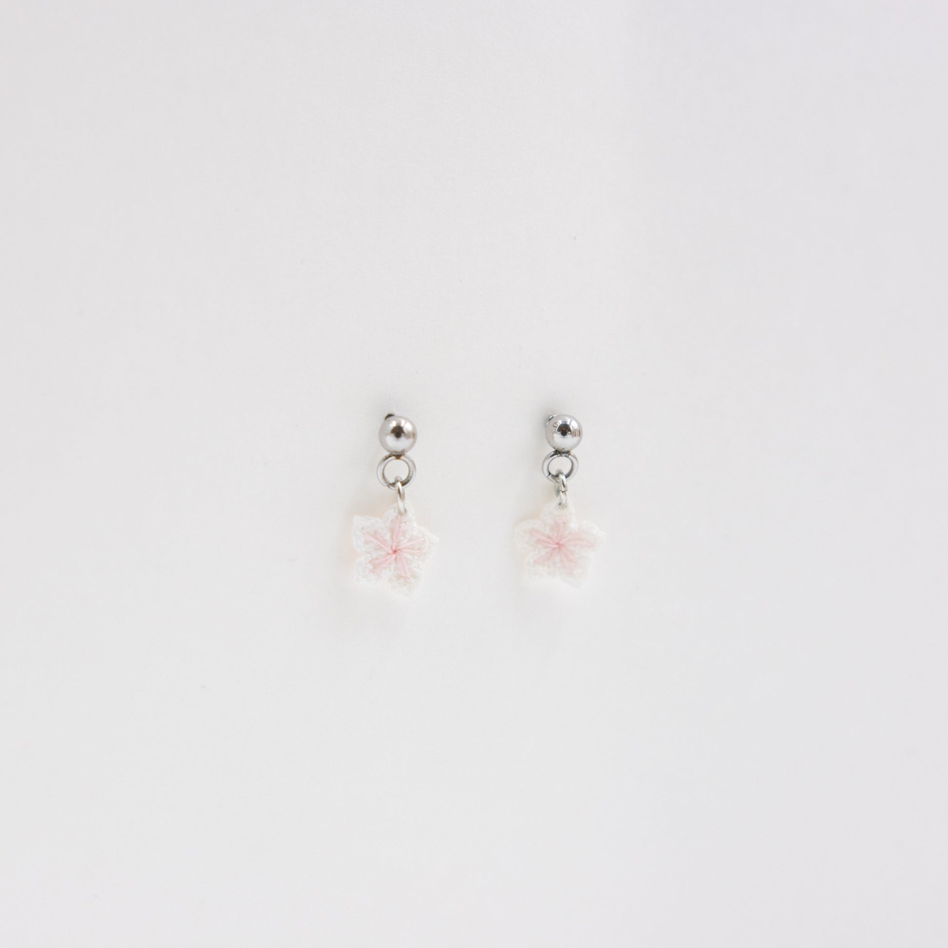 Pair of silver earrings with pink floral charms on a light gray background
