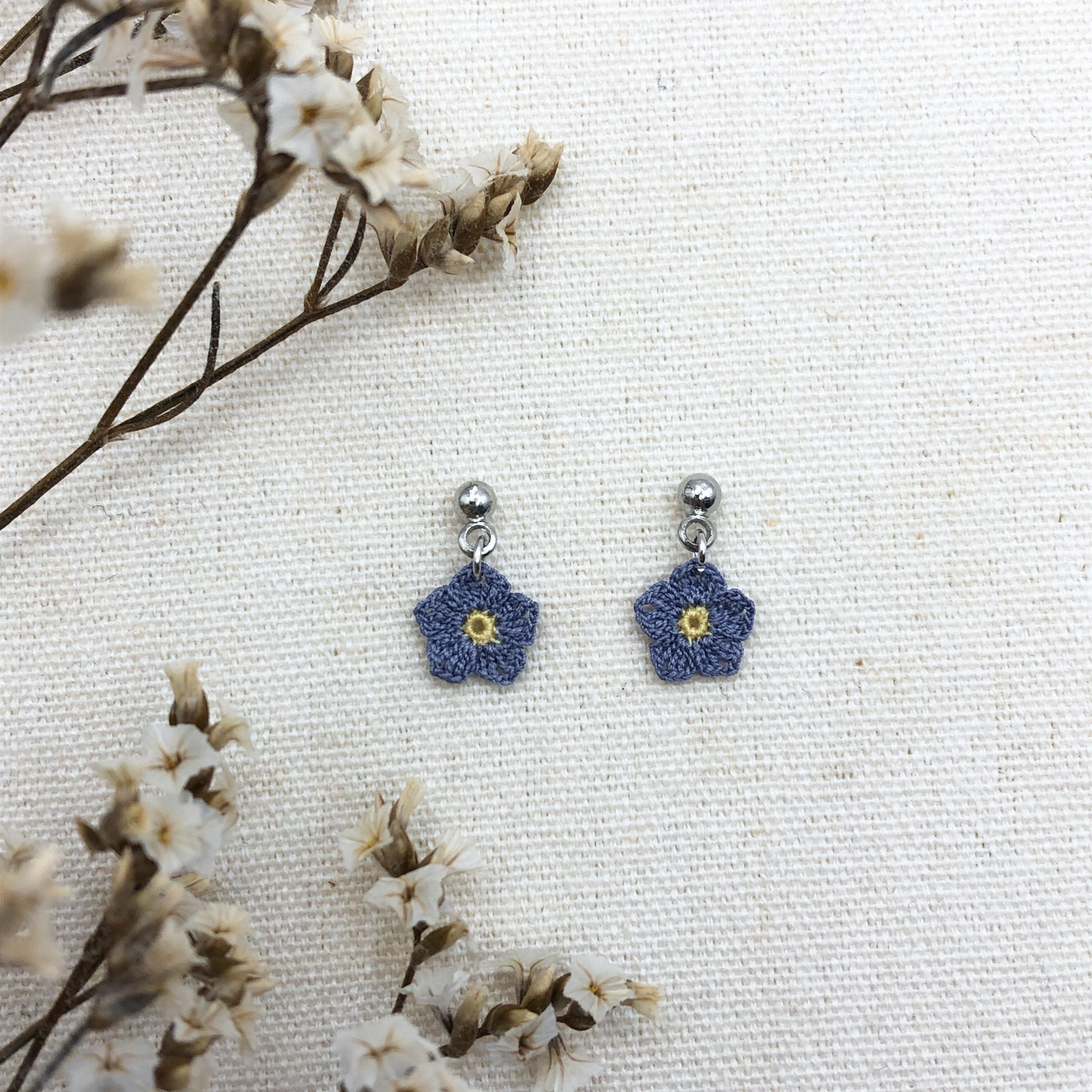 Blue flower-shaped earrings on a white background with dried flowers.